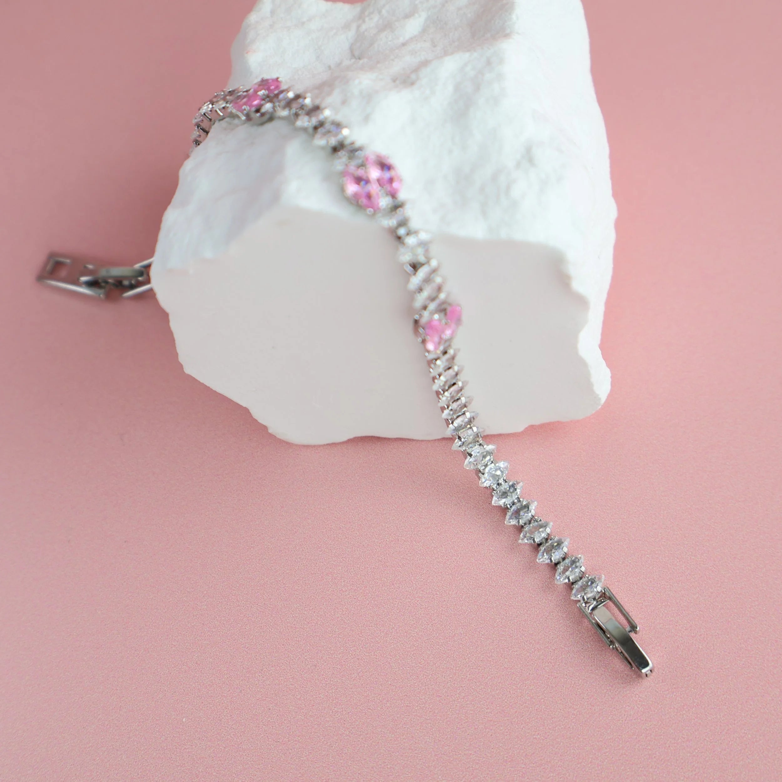 Silver and pink zirconia bracelet displayed on textured white prop
